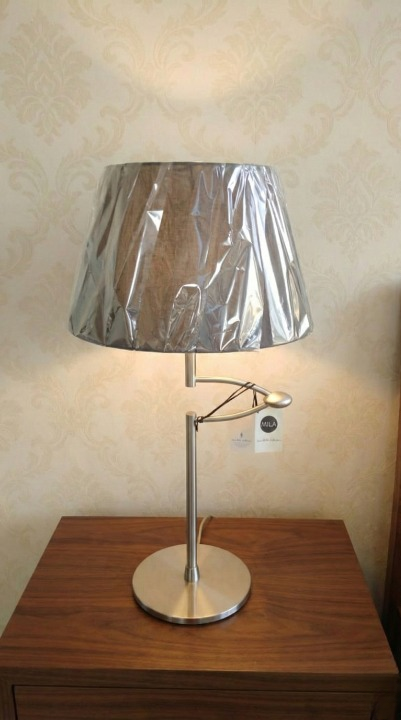 Arlumina Linear Gravity lamp, brushed steel offset pillar base with a dark brown fabric drum shade on a wooden table.